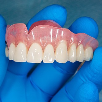 Closeup of blue-gloved hand holding upper arch of dentures