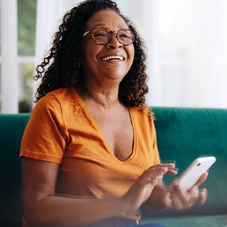 Woman in orange shirt with glasses smiling while tapping her phone