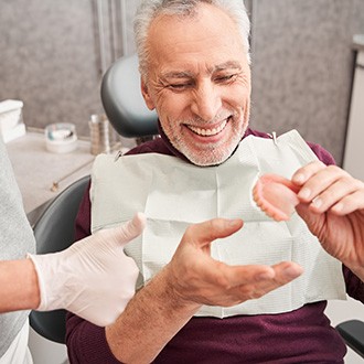 An older man closely assessing dentures handed to him by a dentist