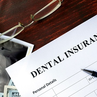 A dental insurance form sitting on a brown desk next to glasses