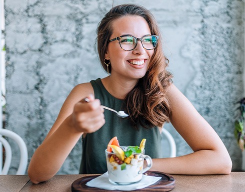 Woman with glasses smiling while eating breakfast