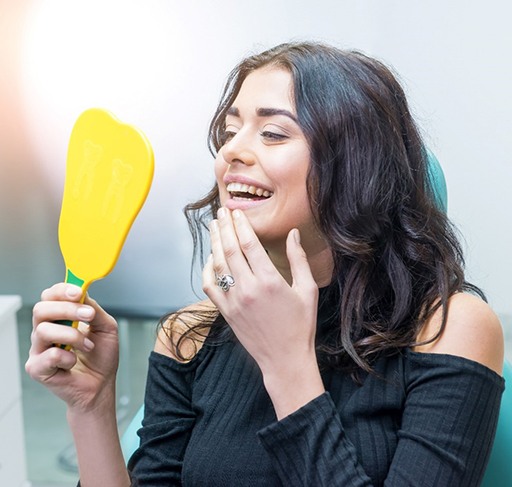 Woman smiling at reflection in handheld mirror