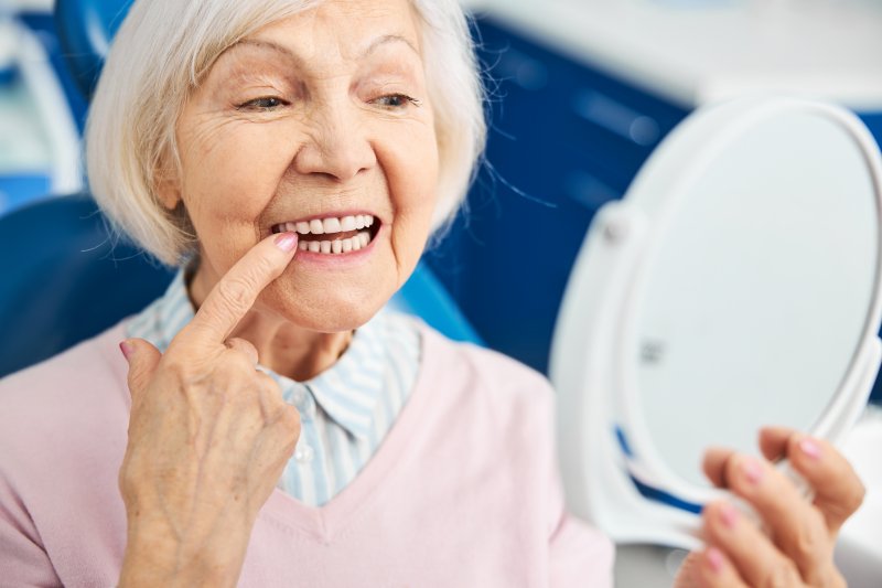 An older woman checking her teeth with a hand mirror