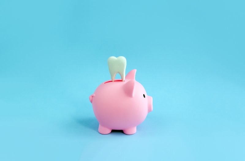 A decorative tooth sitting on top of a pink piggy bank